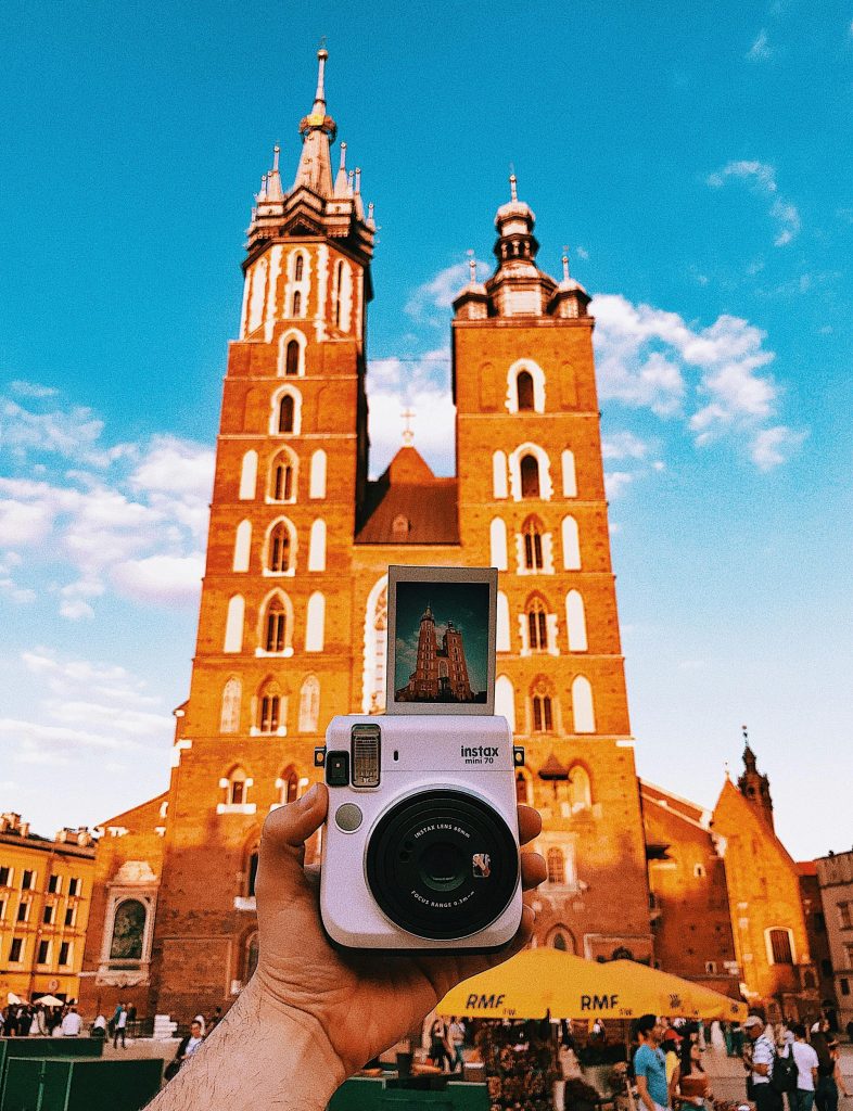 A hand holding a Polaroid camera captures St. Mary's Basilica in Krakow's Main Square, highlighting travel and culture.