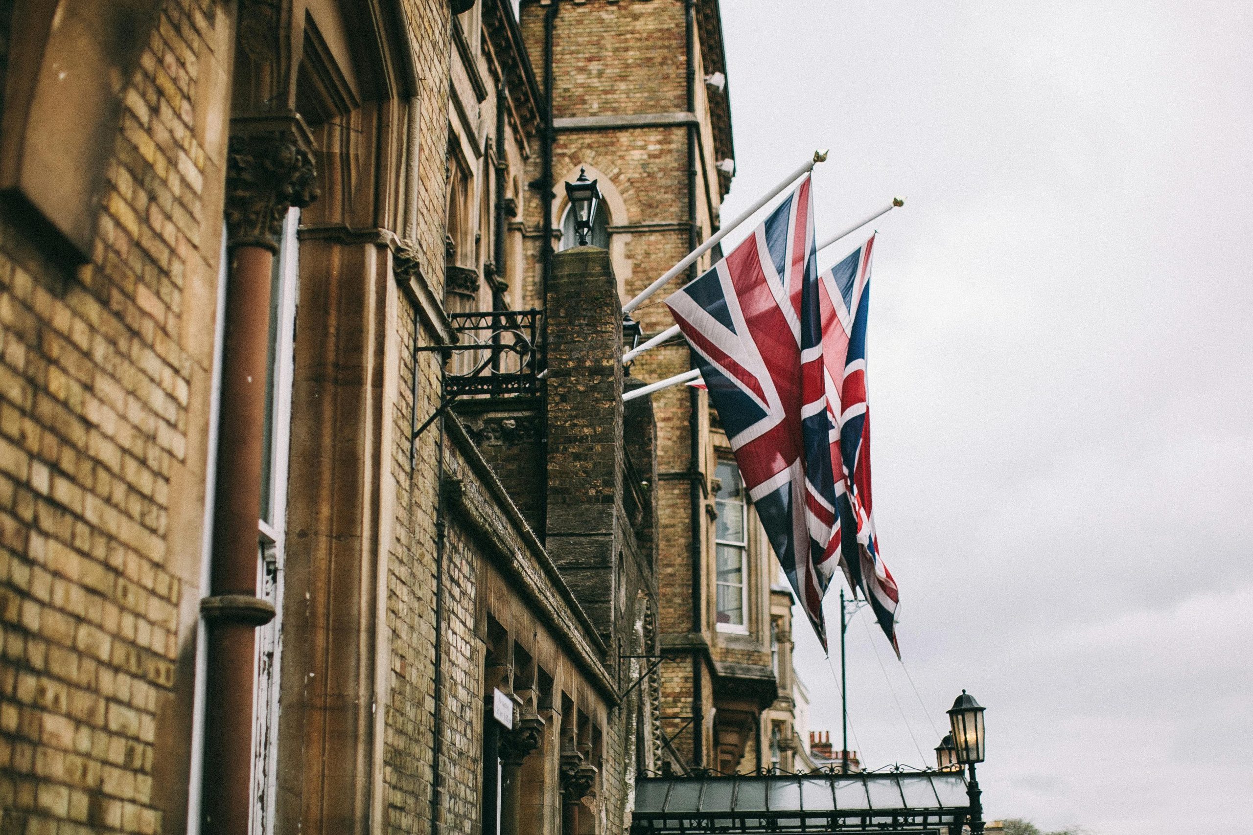 Union Jack flags adorning a historic brick building in Oxford, UK, on a cloudy day.